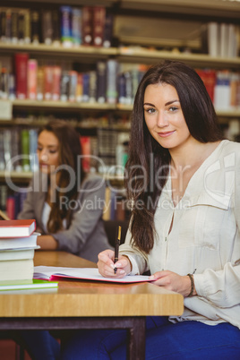 Happy student sitting at desk writing smiling at camera