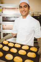 Baker smiling at camera holding tray of rolls