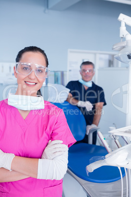 Smiling assistant and dentist behind her with protective glasses