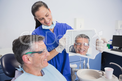 Smiling dentist showing teeth of her patient with a mirror