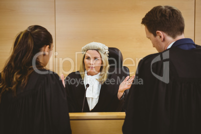 Judge wearing a dress and a wig speaking with lawyers