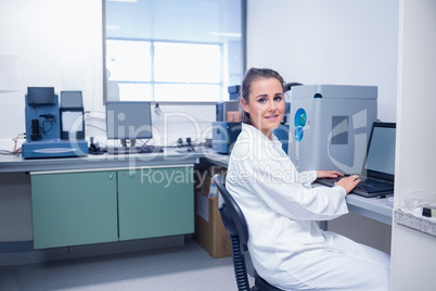 Smiling young biochemist using laptop at her desk