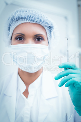 Female dentist in surgical mask holding hook