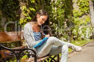 Smiling student sitting on bench and writing on notepad