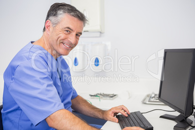 Smiling dentist sitting and using computer