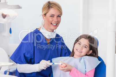 Smiling dentist teaching to her young patient how use toothbrush