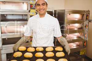 Baker smiling at camera holding tray of rolls