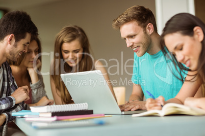 Smiling friends sitting studying and using laptop