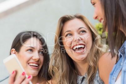 Happy students looking at smartphone outside on campus