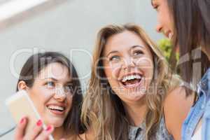 Happy students looking at smartphone outside on campus