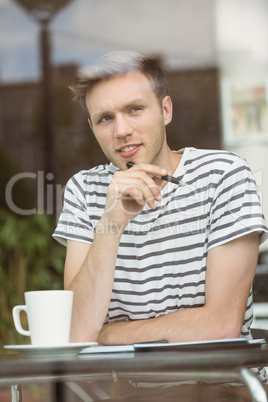 Thinking student sitting with a hot drink and holding a pen