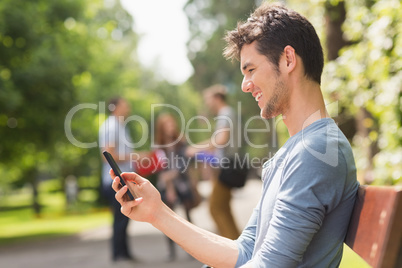 Handsome student sending a text outside