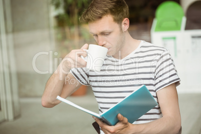 Student drinking a hot drink and holding book