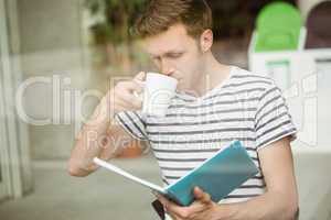 Student drinking a hot drink and holding book
