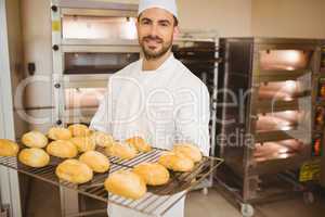 Baker smiling at camera holding rack of rolls