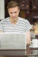 Smiling student sitting with a hot drink using laptop