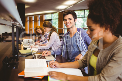 Student looking at camera while studying with classmates Student looking at camera while studying with classmates