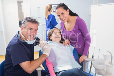 Smiling pediatric dentist with a happy young patient and her mot