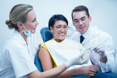 Dentist with assistant showing woman how to brush teeth