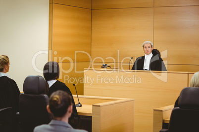 Unsmiling judge wearing wig with american flag behind him