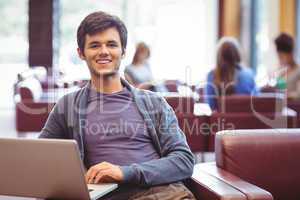 Happy young student sitting on couch using laptop