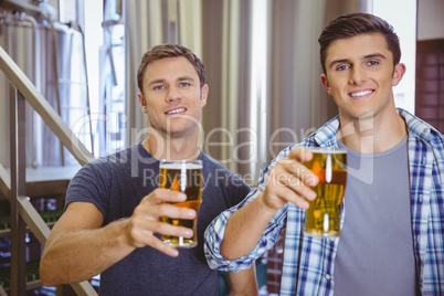 Young men holding a pint of beer smiling at camera