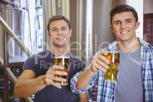 Young men holding a pint of beer smiling at camera