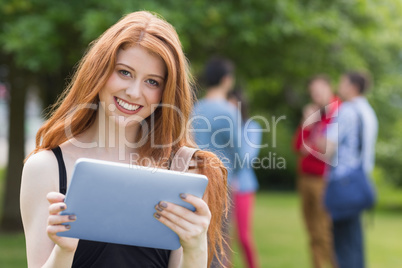 Pretty student smiling at camera using tablet pc