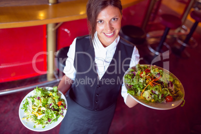 Pretty barmaid holding plates of salads