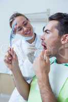 Man looking at mirror by female dentist