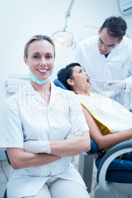 Smiling female dentist with assistant examining womans teeth