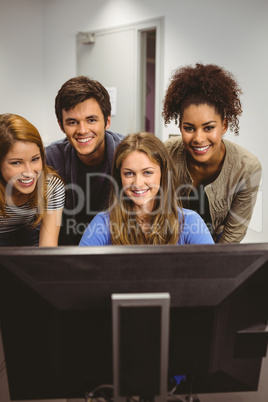 Smiling students using computer together looking at camera