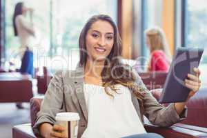 Smiling girl using digital tablet and holding disposable cup