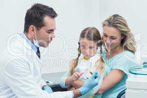 Dentist with assistant teaching girl how to brush teeth