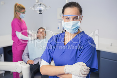 Dentist wearing surgical mask and safety glasses arms crossed