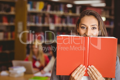 Pretty brunette student holding book in front of her face