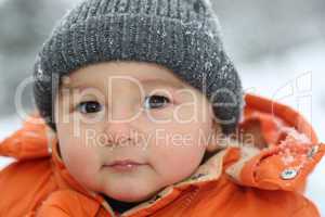 Baby im Schnee im Winter mit Mütze schaut in die Kamera