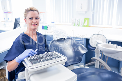 Dentist sitting with tray of tools smiling at camera