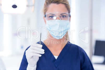 Dentist in mask holding dental explorer