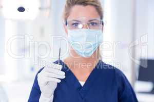 Dentist in mask holding dental explorer