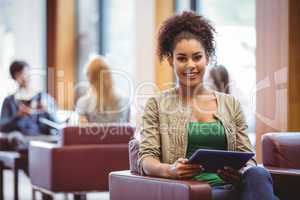 Student sitting on sofa using her tablet pc smiling at camera