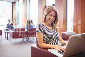Happy young student sitting on couch using laptop