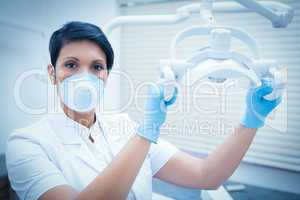 Demale dentist in surgical mask adjusting light