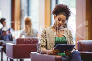 Focused student sitting on sofa using her tablet pc