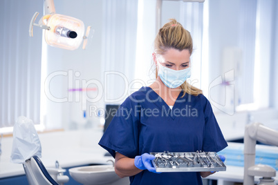 Dentist in mask holding tray of tools