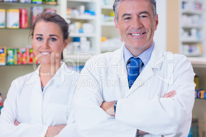 Smiling pharmacist and his trainee with arms crossed