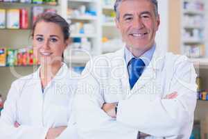 Smiling pharmacist and his trainee with arms crossed