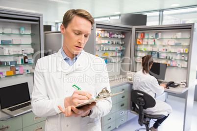 Focused pharmacist writing on clipboard Focused pharmacist writing on clipboard
