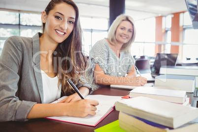 Smiling matures females students writing notes at desk