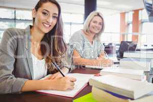 Smiling matures females students writing notes at desk